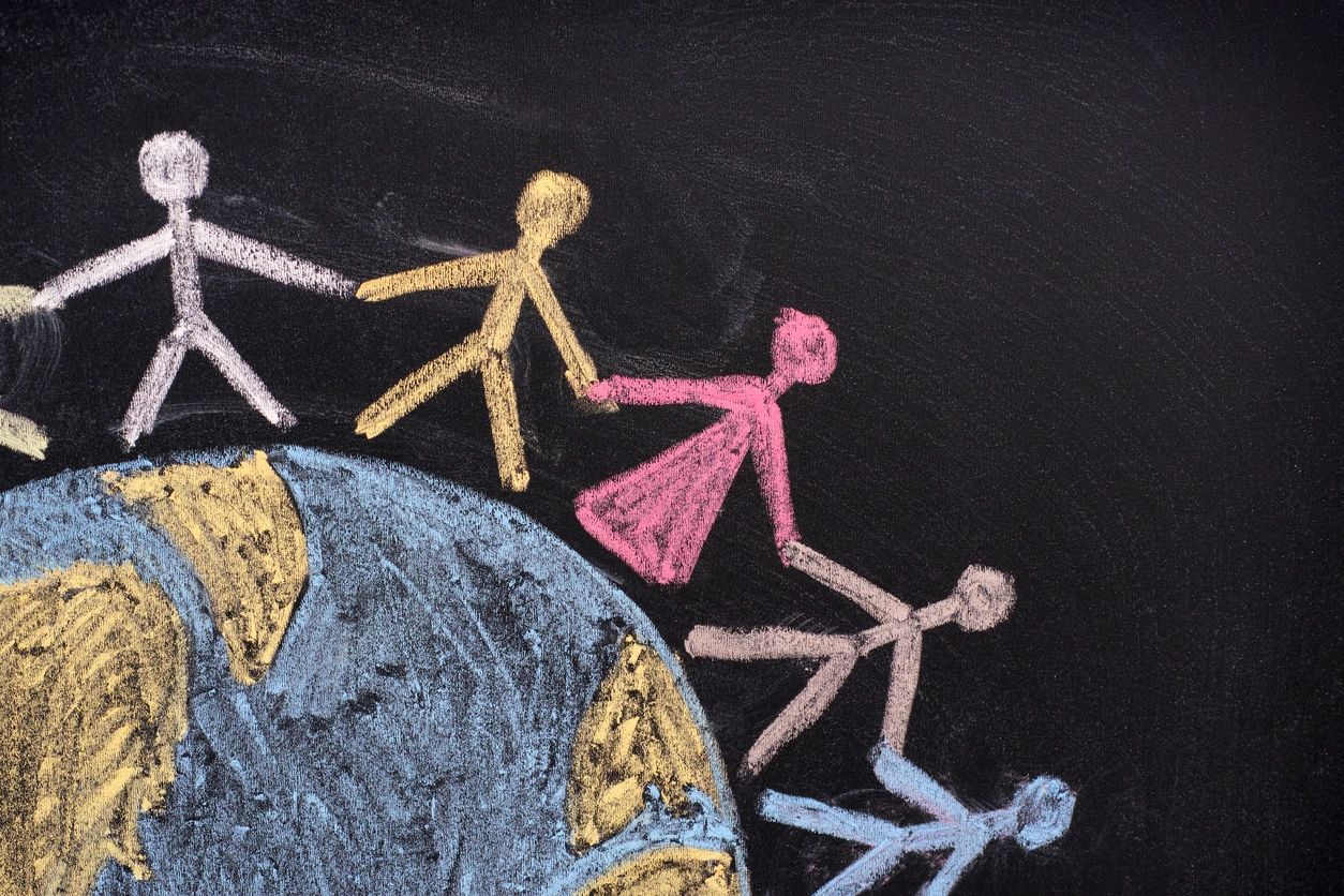 A chalkboard drawing of stick figure children holding hands and standing on top of the globe
