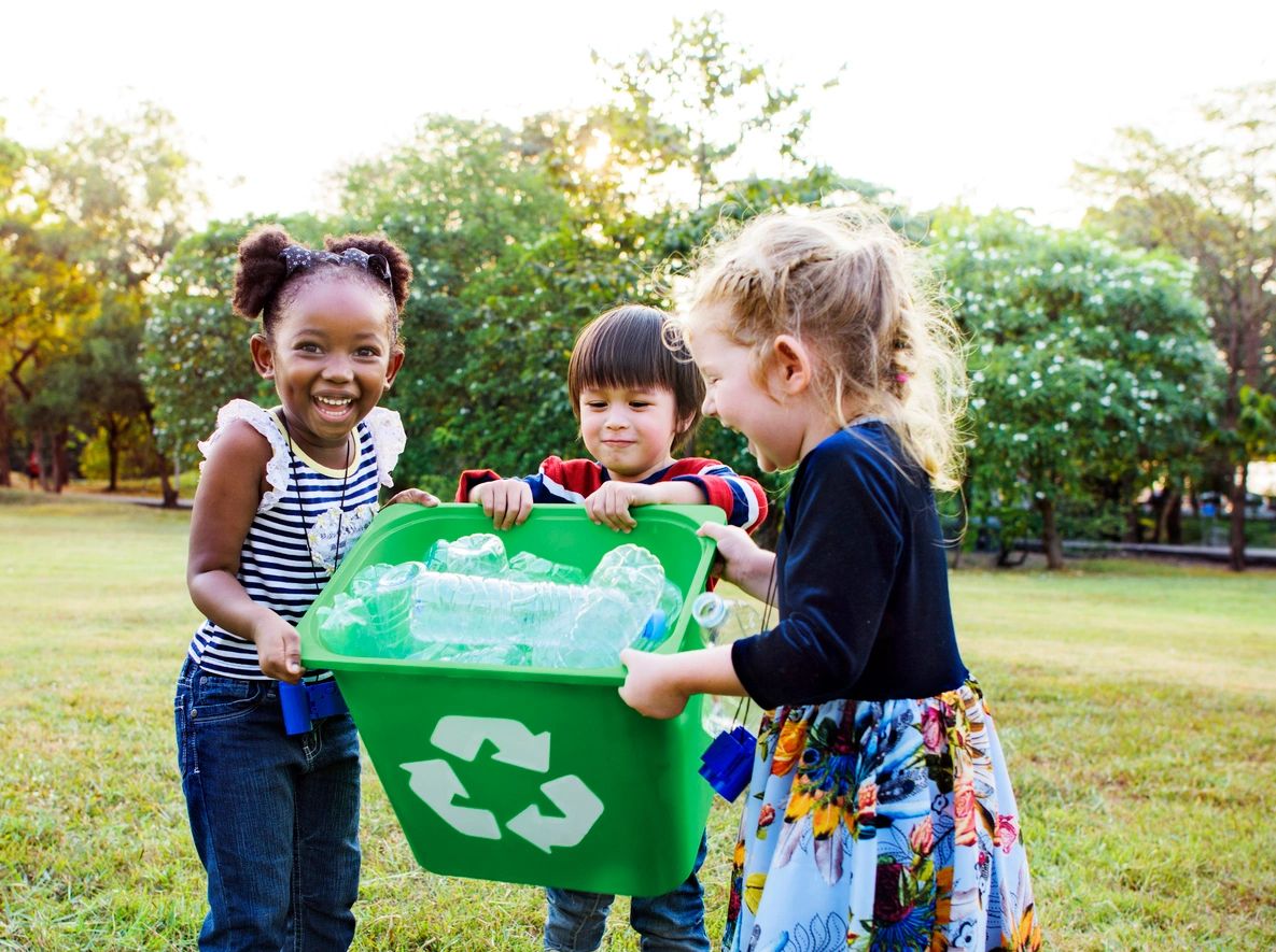 Three children holding a recycling bin filled with plastic bottles